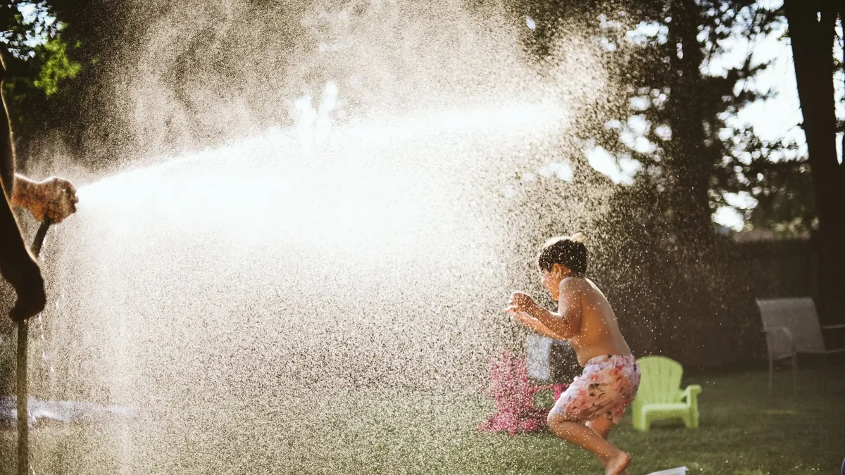 Enfants qui rient en jouant avec de l'eau dans un jardin pendant la canicule