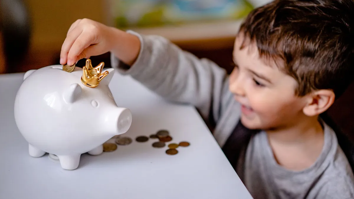 Enfant souriant qui met des pièces dans sa tirelire pour apprendre à gérer l'argent