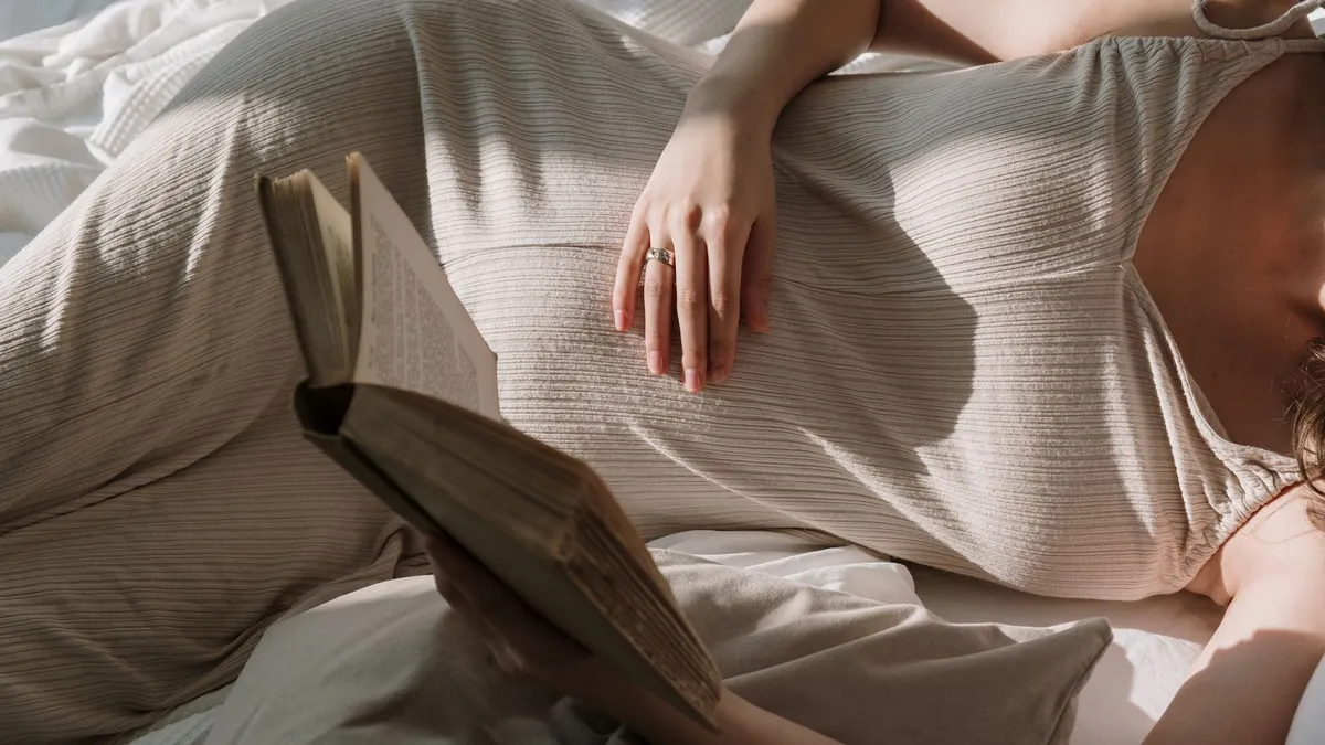 Femme enceinte confortablement installée en train de lire un livre de grossesse