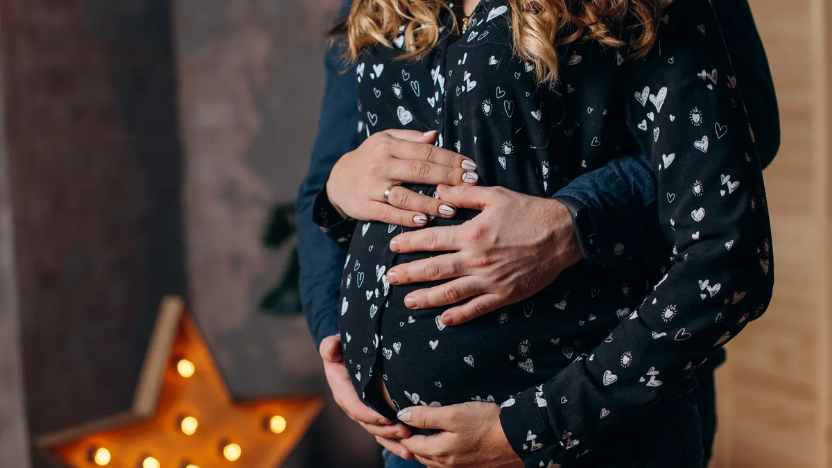Futur papa qui pose tendrement les mains sur le ventre arrondi de sa compagne