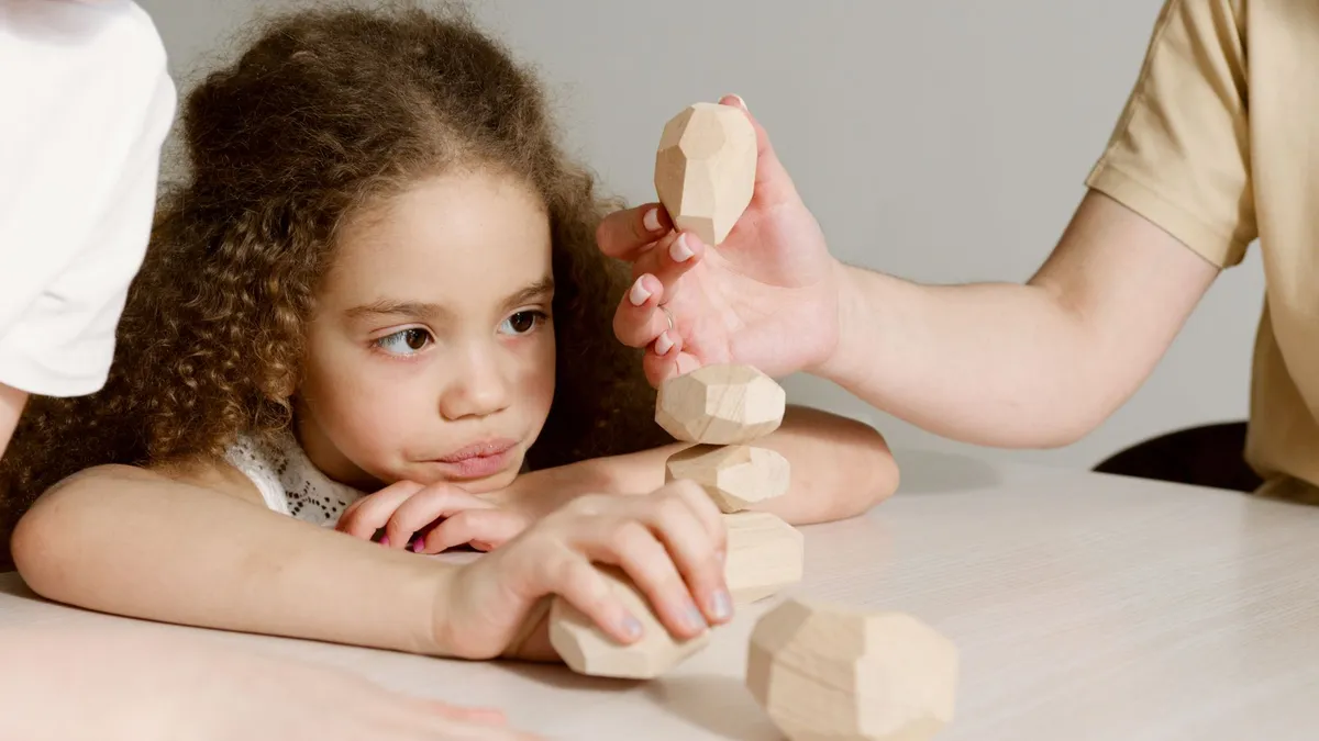 Jeune enfant concentré en train d'empiler des jouets en bois, dans l'esprit Montessori